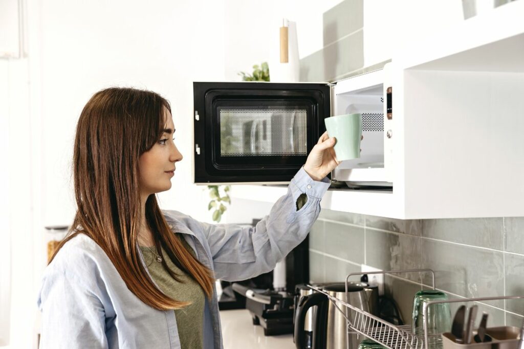 woman placing a cup of water in an empty microwave