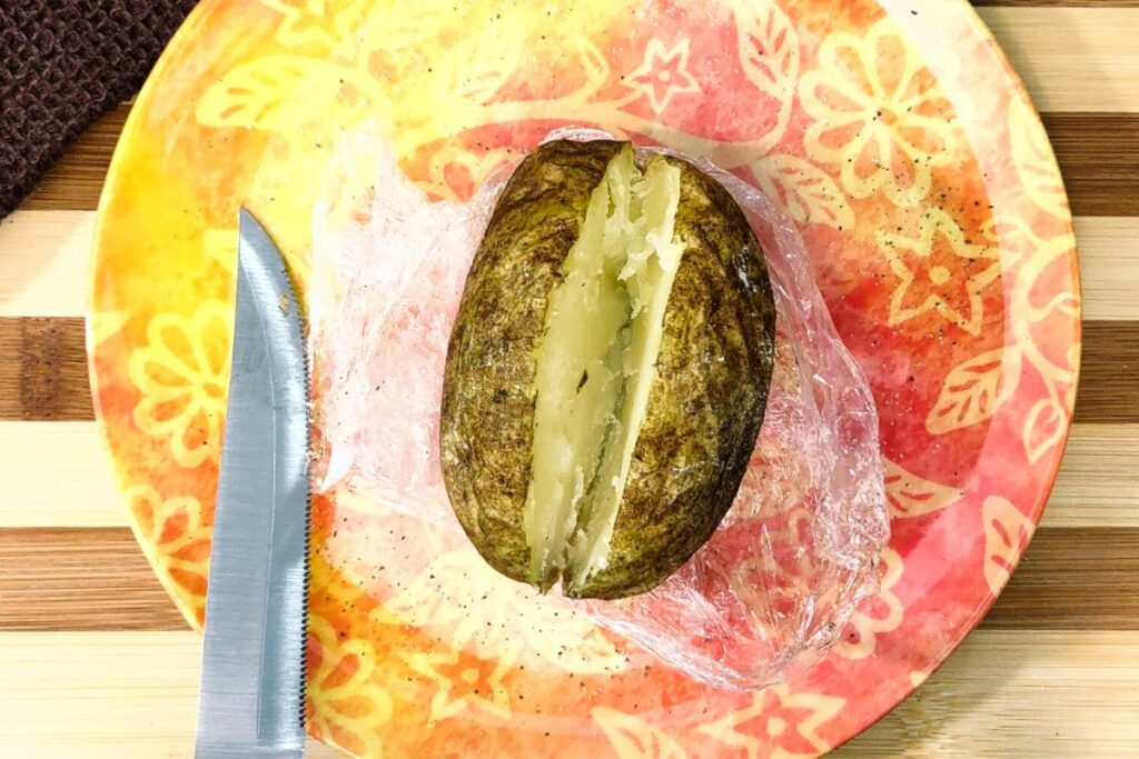 carefully unwrap plastic wrap and slice baked potato with a knife