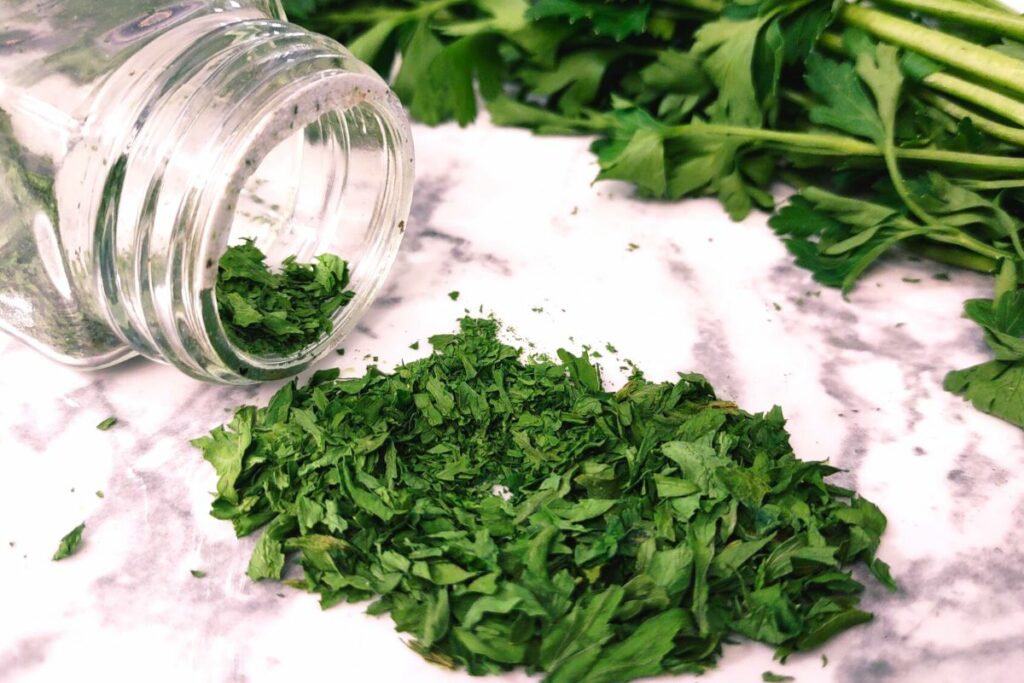 dehydrated parsley leaves pouring out of a glass spice jar
