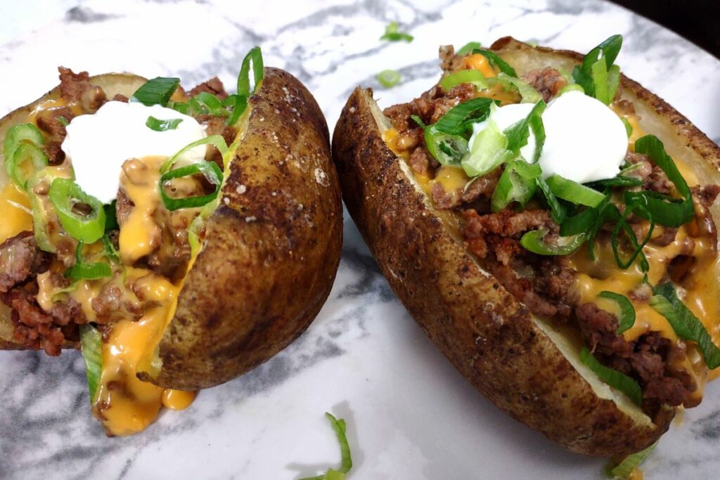 closeup of reheated baked potatoes with beef, melted queso, sour cream, and green onions