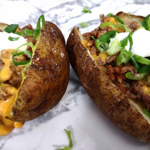 closeup of reheated baked potatoes with beef, melted queso, sour cream, and green onions