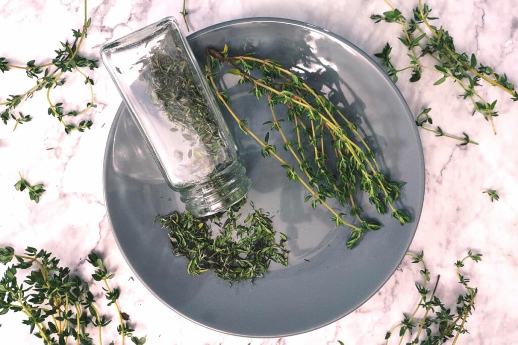 overhead shot of microwave dried thyme spilling out of glass jar with stems to the side