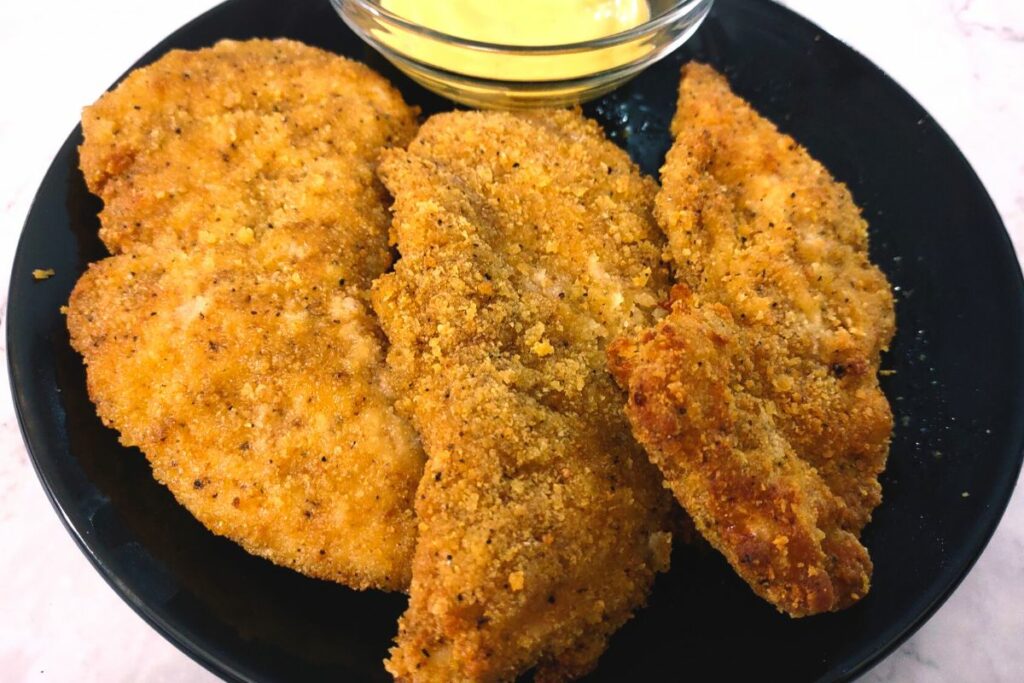 3 air fryer chicken fingers on a plate with dipping sauce