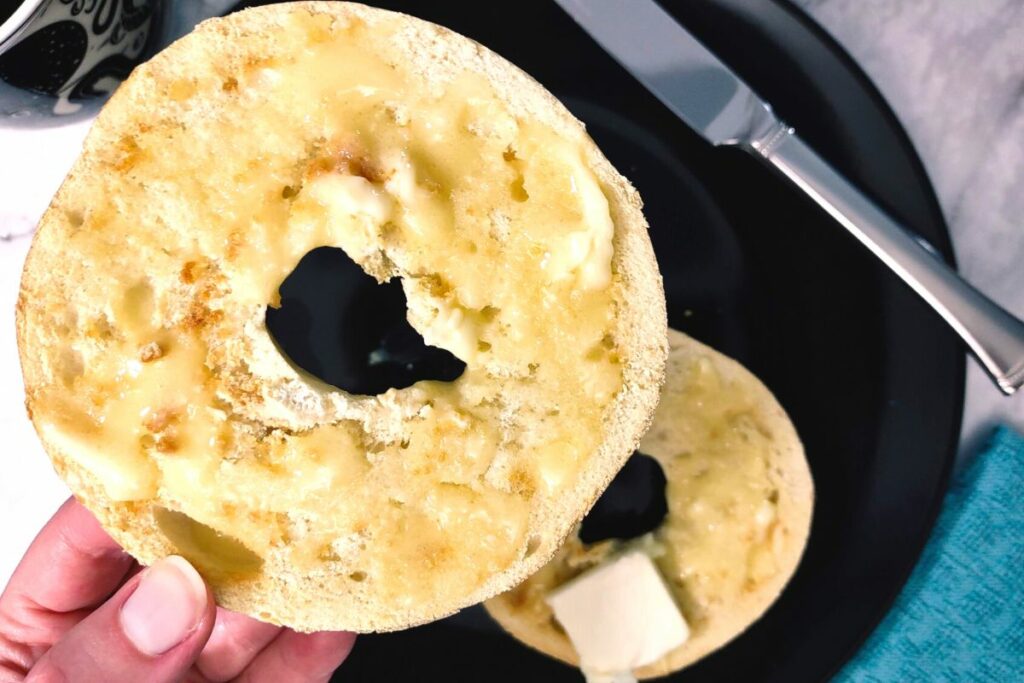closeup holding a toasted bagel with butter
