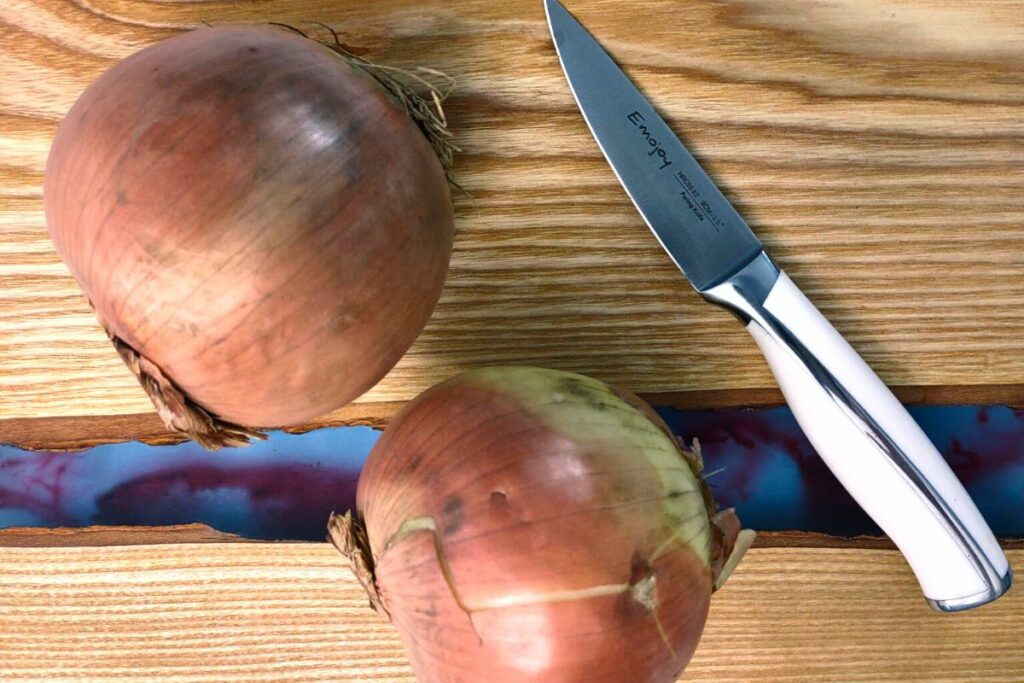 two whole onions on a cutting board with a knife