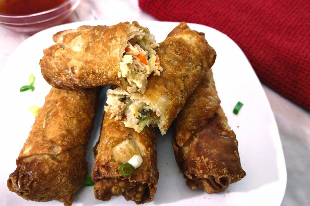 closeup of crispy air fryer egg rolls on a plate stacked with one open