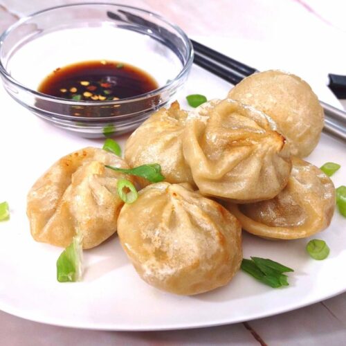 delicious air fried bibigo dumplings stacked on a plate with soy sauce and chopsticks