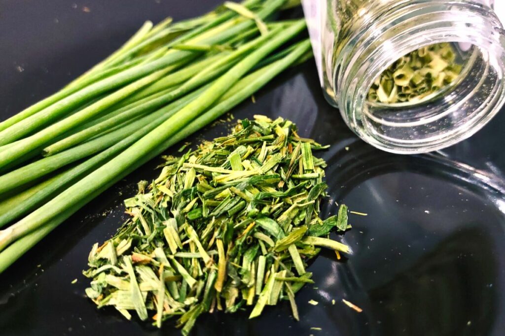 closeup of dried and chopped chives on a plate with fresh chive stalks