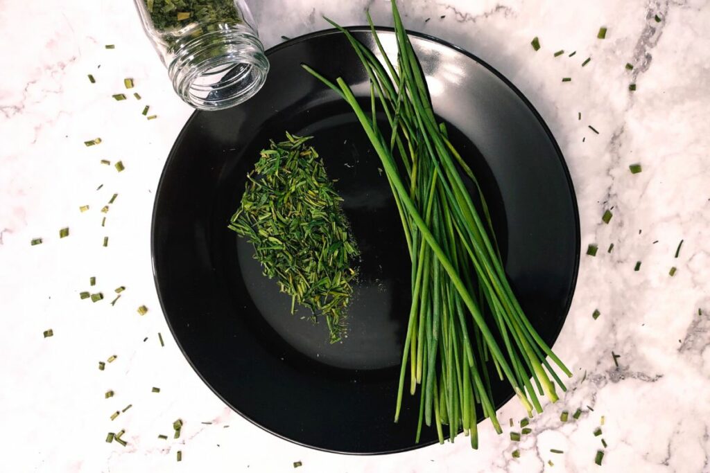 dried chives on a plate spilling out of glass spice jar
