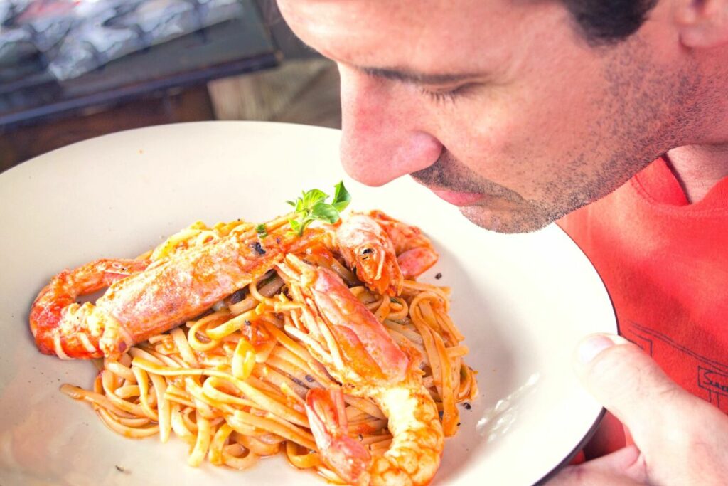 man smelling a bowl of cooked shrimp on top of pasta