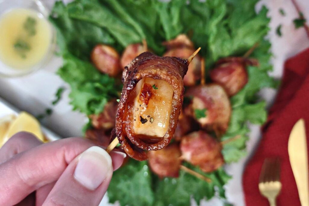closeup holding bacon wrapped scallop on a toothpick
