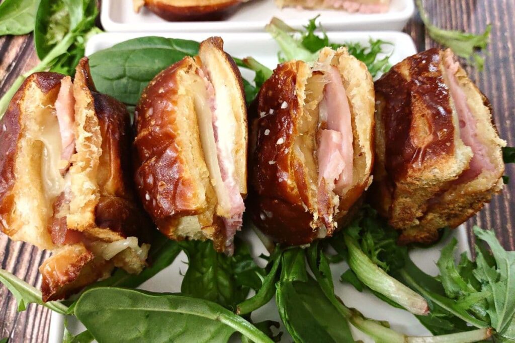 four ham and cheese sliders on their side sitting horizontal on a plate with greens