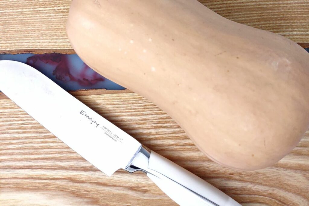 fresh full butternut squash on a cutting board with a knife