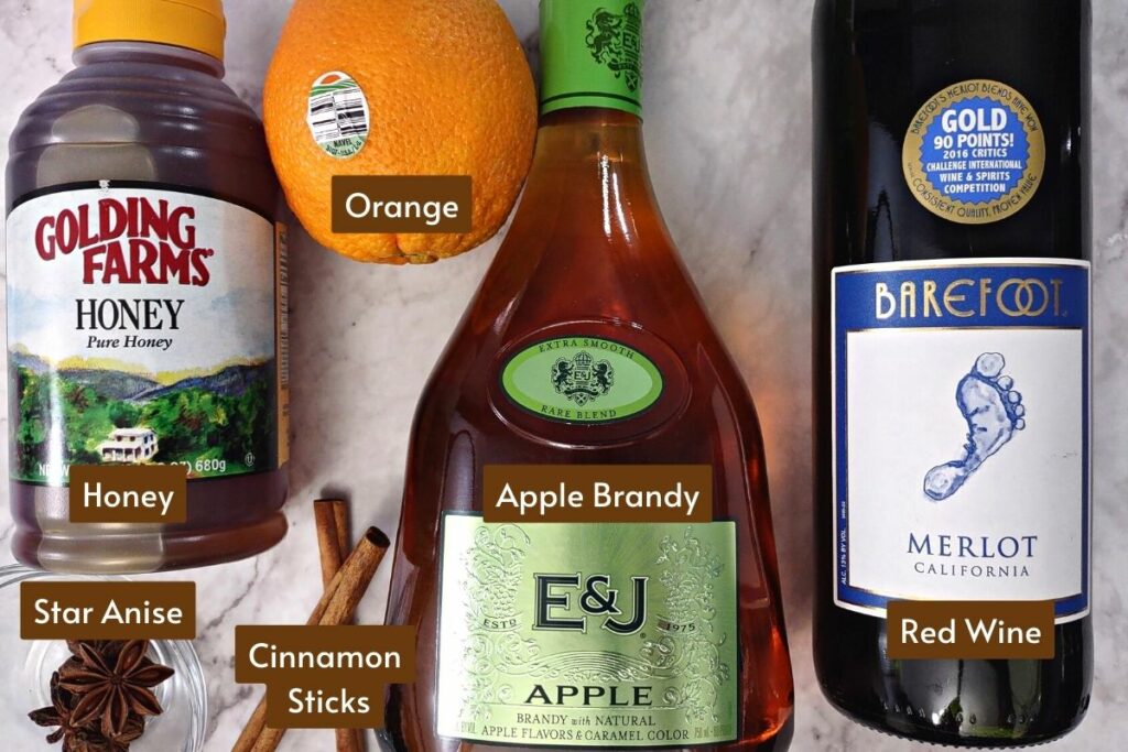 microwave mulled wine ingredients: red wine, apple brandy, honey, cinnamon sticks, star anise, and an orange