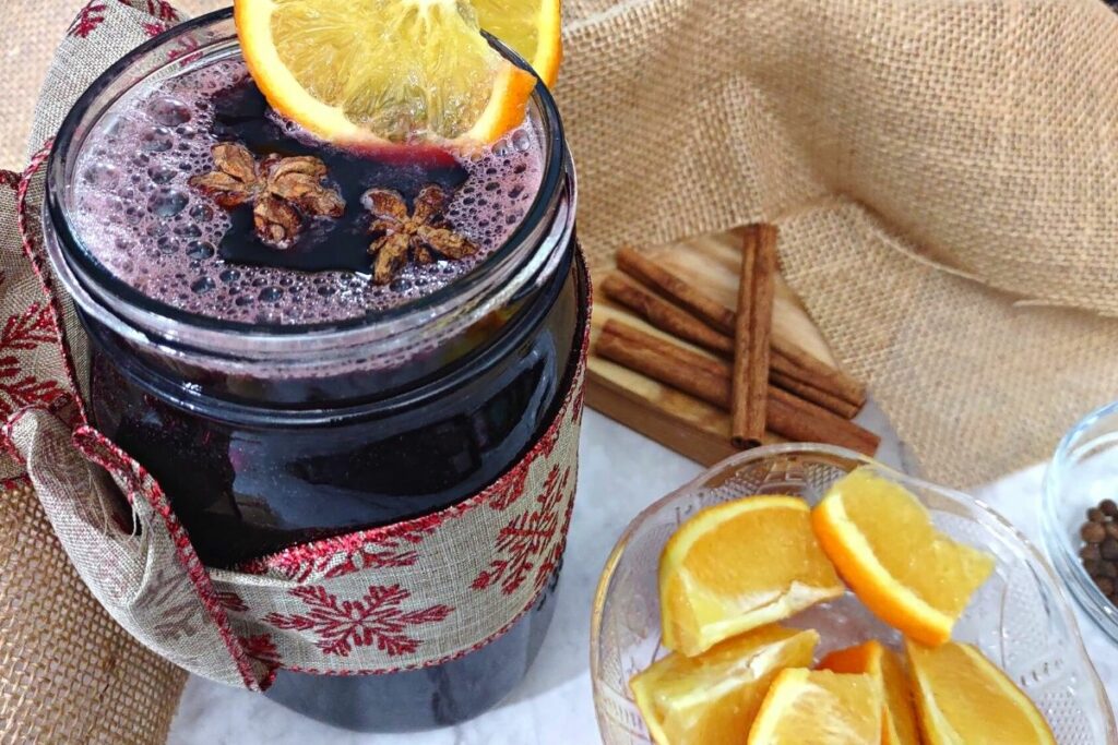 mason jar filled with mulled wine next to a bowl of orange slices and cinnamon sticks