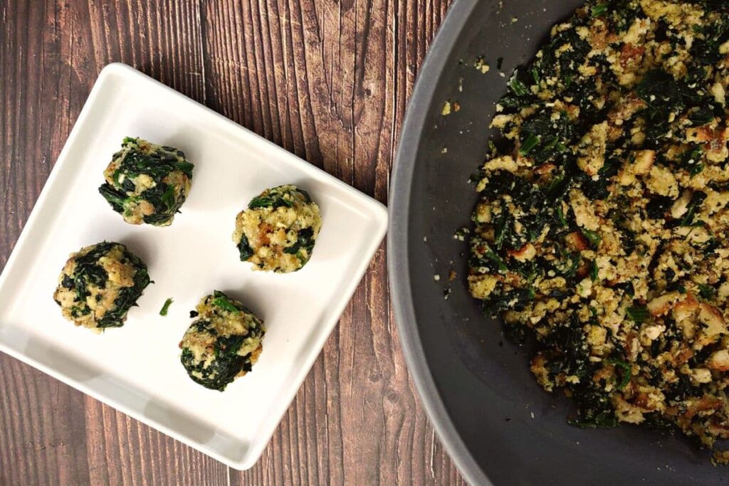 four rolled spinach balls on a square plate to the left with the large bowl of mixture to the right