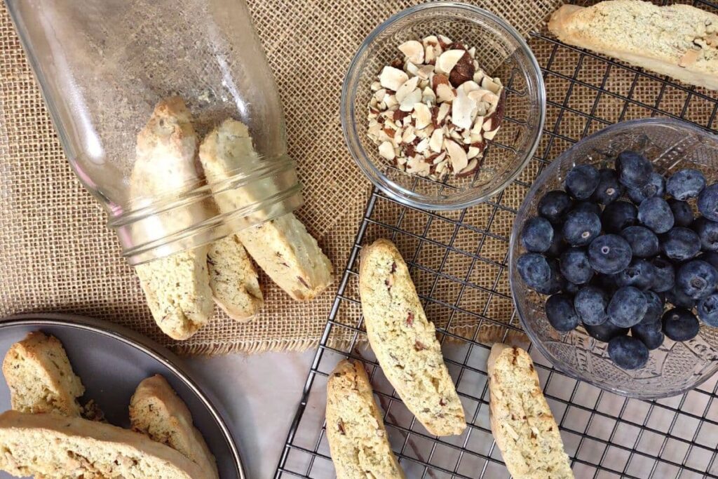 overhead view of orange and almond biscotti on a wire rack with sliced almonds and blueberries on the side