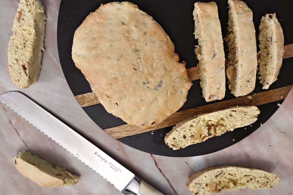 partially air fried biscotti being cut into 1 inch slices on a circular cutting board