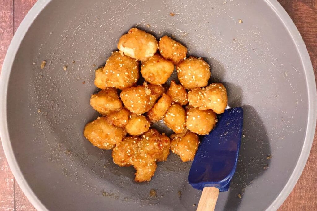 air fryer cauliflower being mixed with buffalo sauce in a bowl