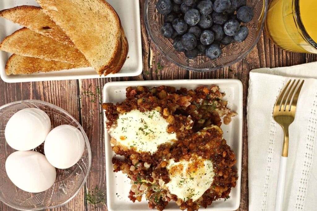 overhead view of air fryer corned beef hash with eggs on a square plate with toast and fresh fruit