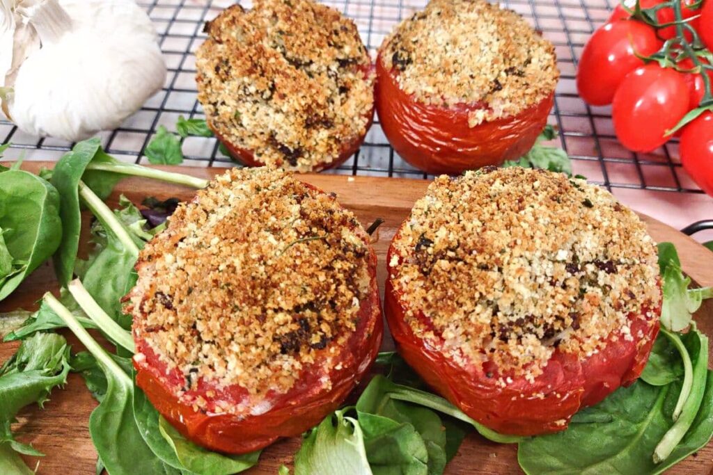 four italian stuffed tomatoes on a bed of basil with fresh garlic in the background