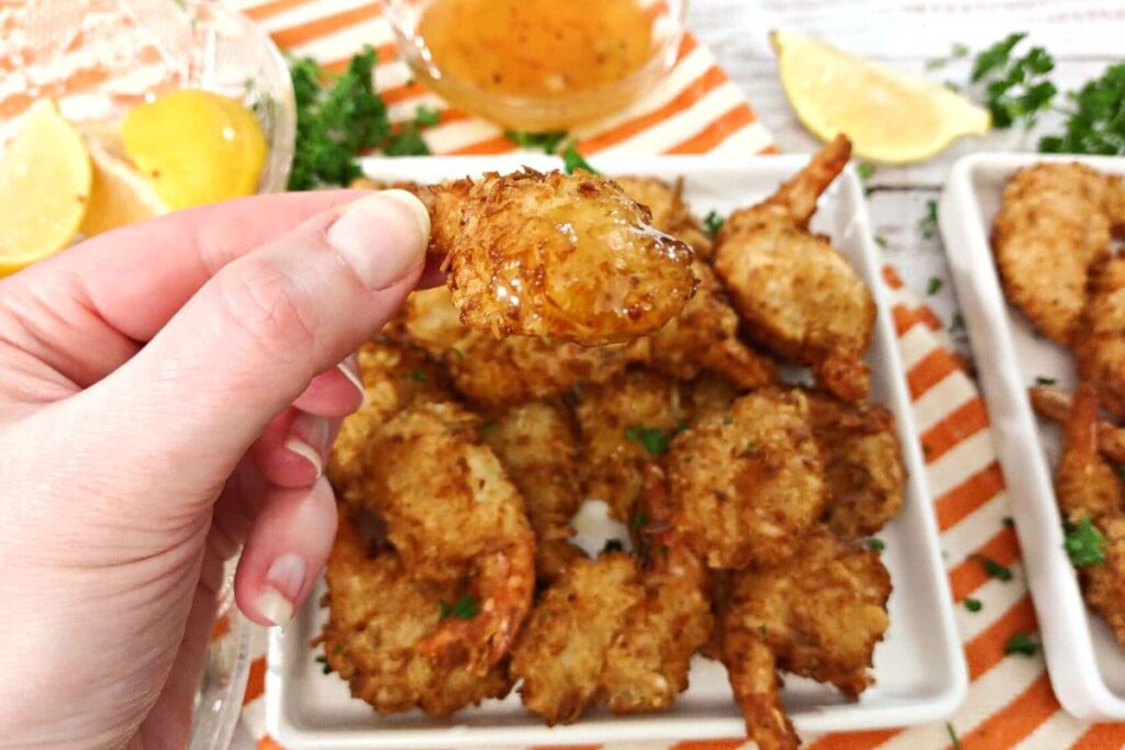 holding an air fried coconut shrimp dipped in duck sauce