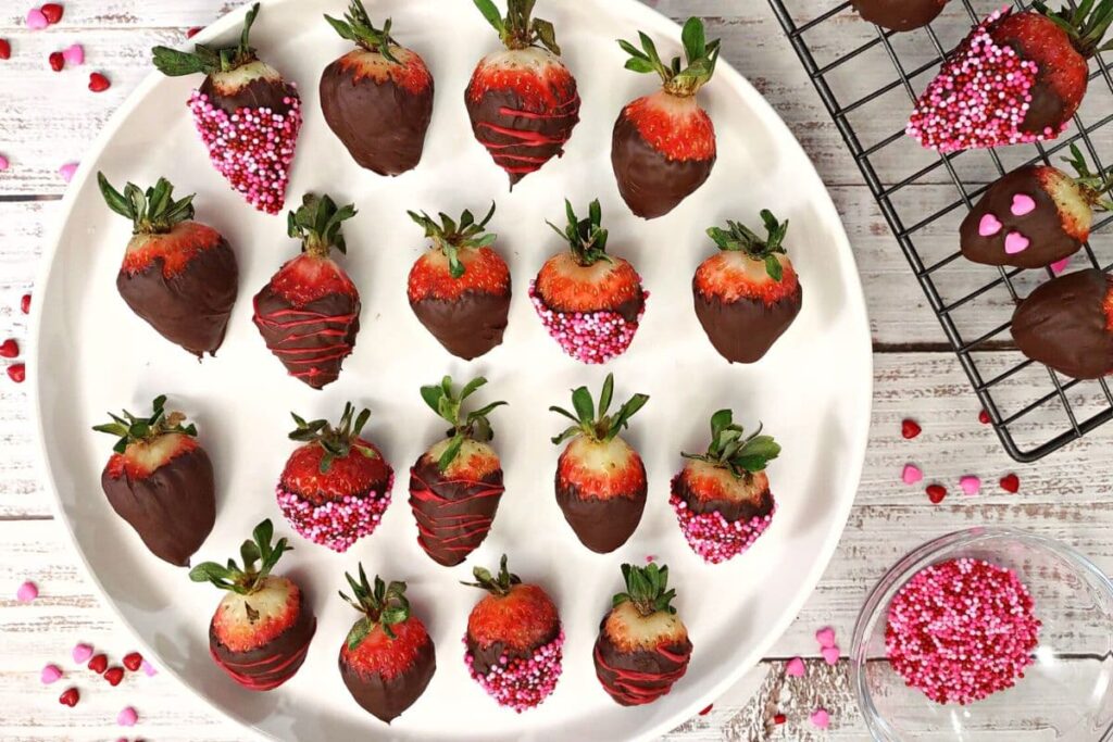 overhead view of chocolate covered strawberries on a white circle plate with some on a wire rack to the right