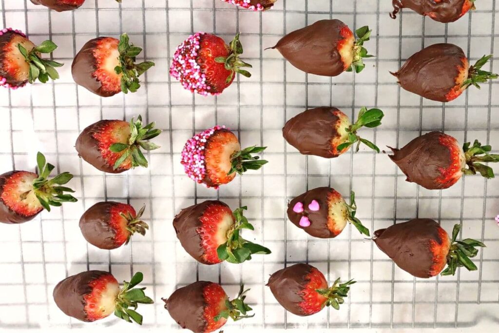 overhead view of chocolate covered strawberries drying on a wax paper lined wire rack