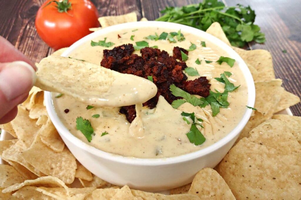 dipping a tortilla chip into queso cheese dip with chorizo
