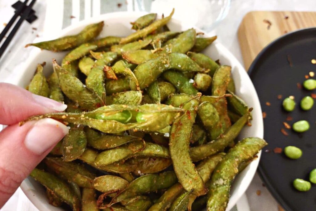 holding up spicy garlic edamame from the air fryer splitting down the middle