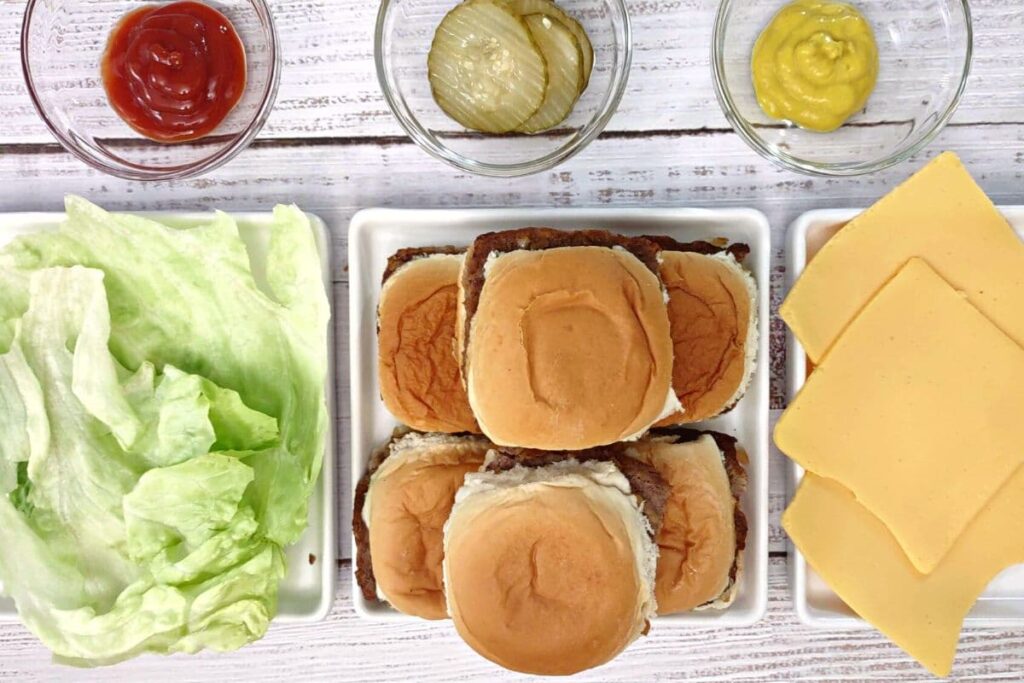 overhead view of white castle sliders on a plate with lettuce, cheese, and condiments surrounding