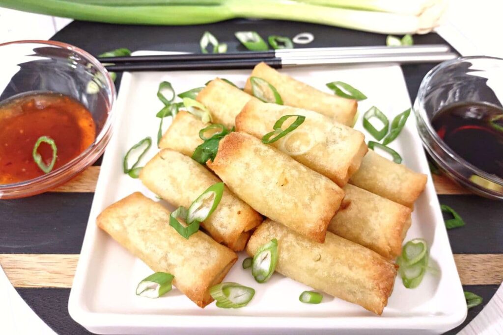 reheated air fryer spring rolls stacked on a plate with dipping sauces on the site