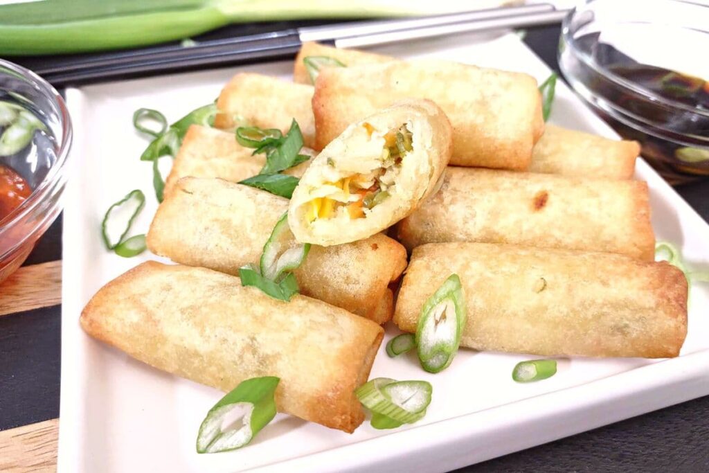reheated air fryer spring rolls stacked on a plate with one cut in half
