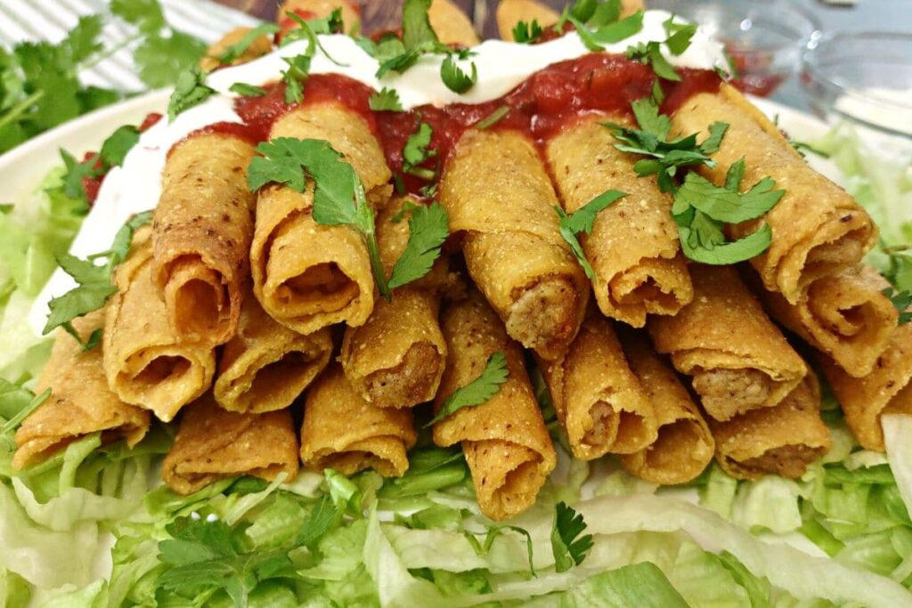 closeup of air fryer chicken taquitos stacked up with salsa and sour cream on top
