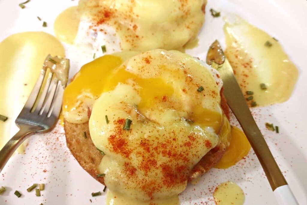 splitting open poached eggs benedict with a knife and fork