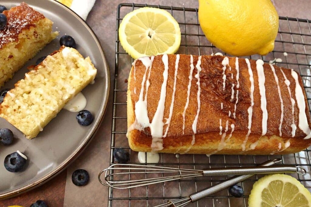 uncut loaf of lemon pound cake with glaze on top next to fresh cut slices
