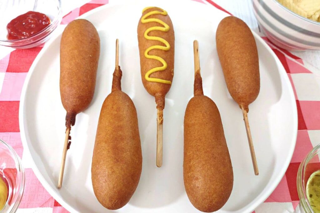 5 air fryer state fair corn dogs on a plate with a mustard squiggle