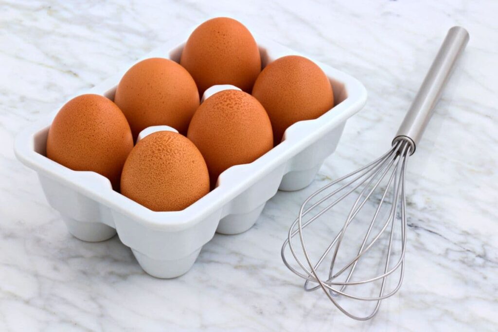 brown eggs in a container next to a whisk