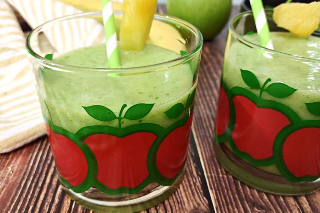 closeup of green apple smoothie in a glass with a pineapple chunk on the rim