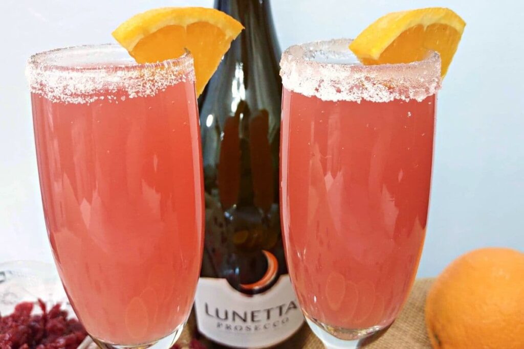 closeup of two cranberry orange mimosas in front of prosecco bottle
