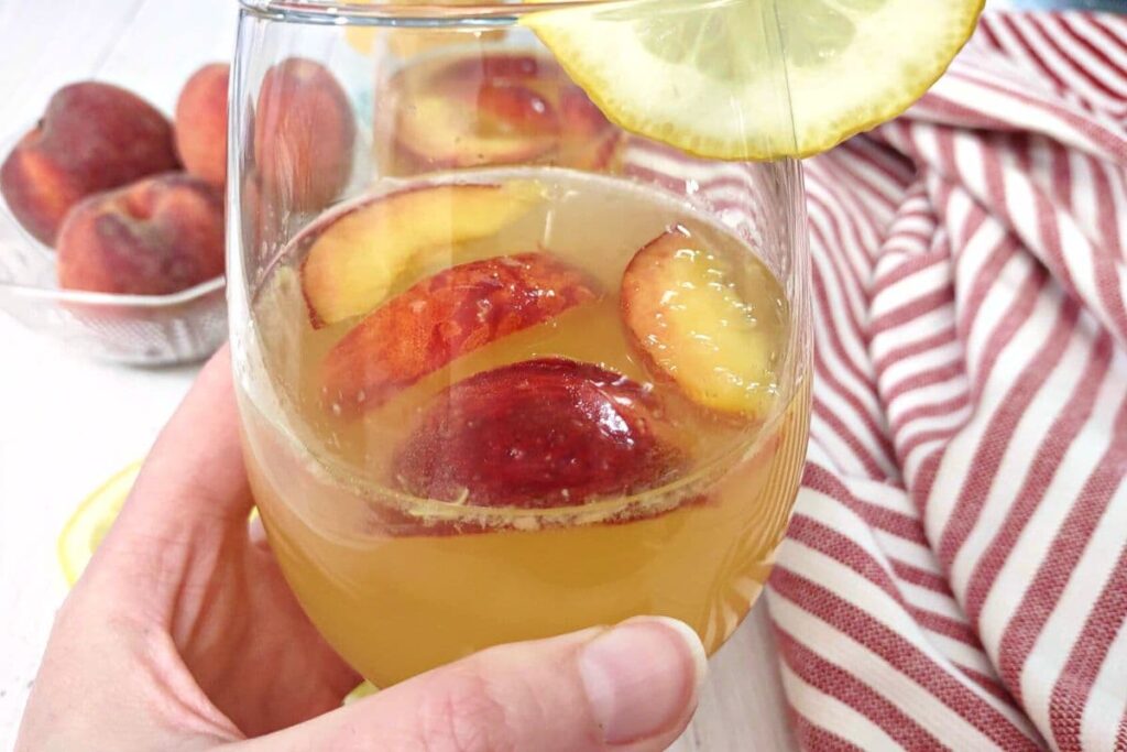 holding up a glass of ginger peach sangria