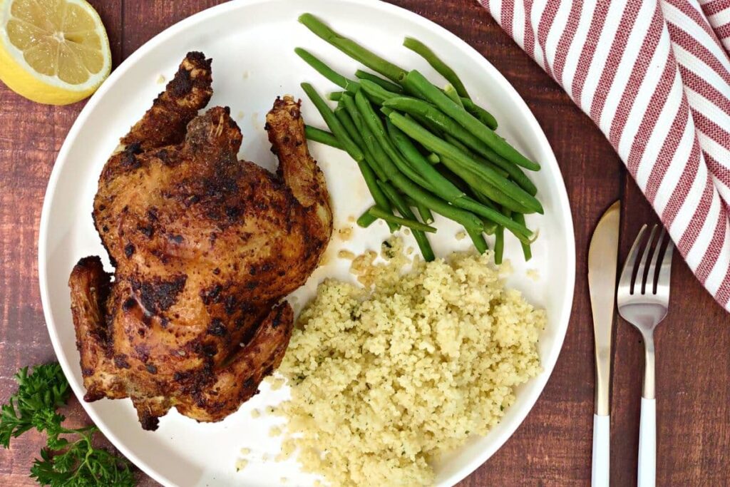 overhead view of air fryer cornish hen on a plate with green beans and couscous