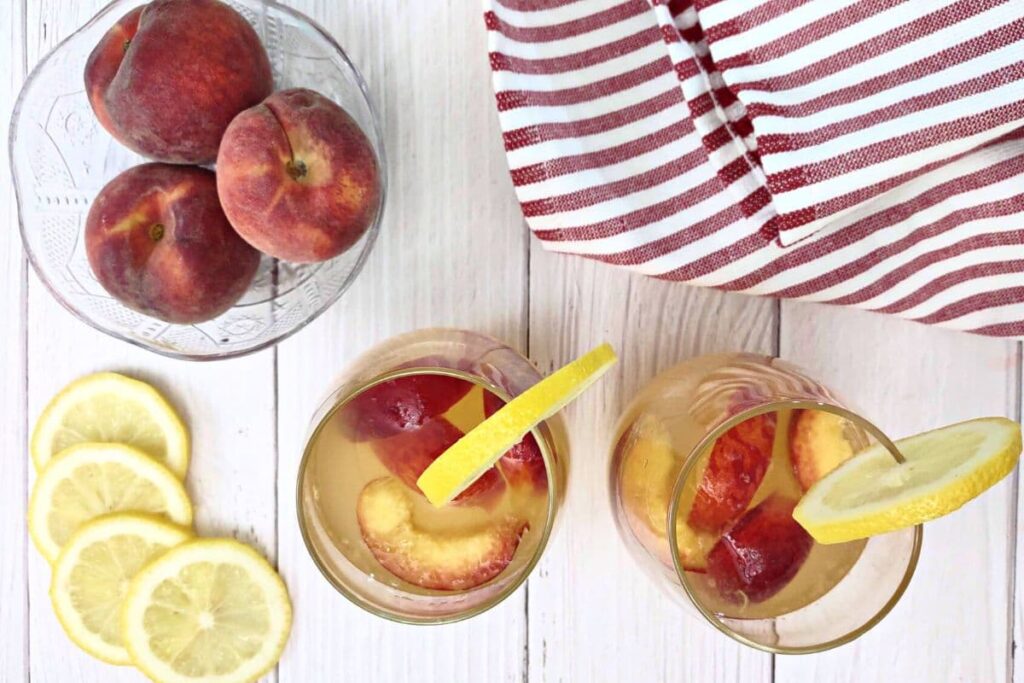 overhead view of two glasses of ginger peach sangria with fresh peaches and lemon slices