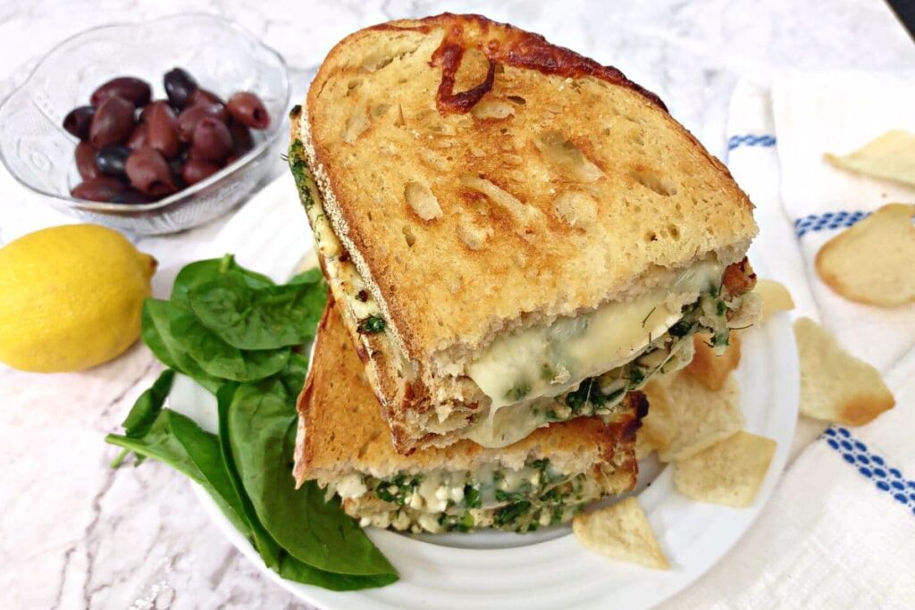 spanakopita grilled cheese halves stacked on top of each other surrounded by veggies