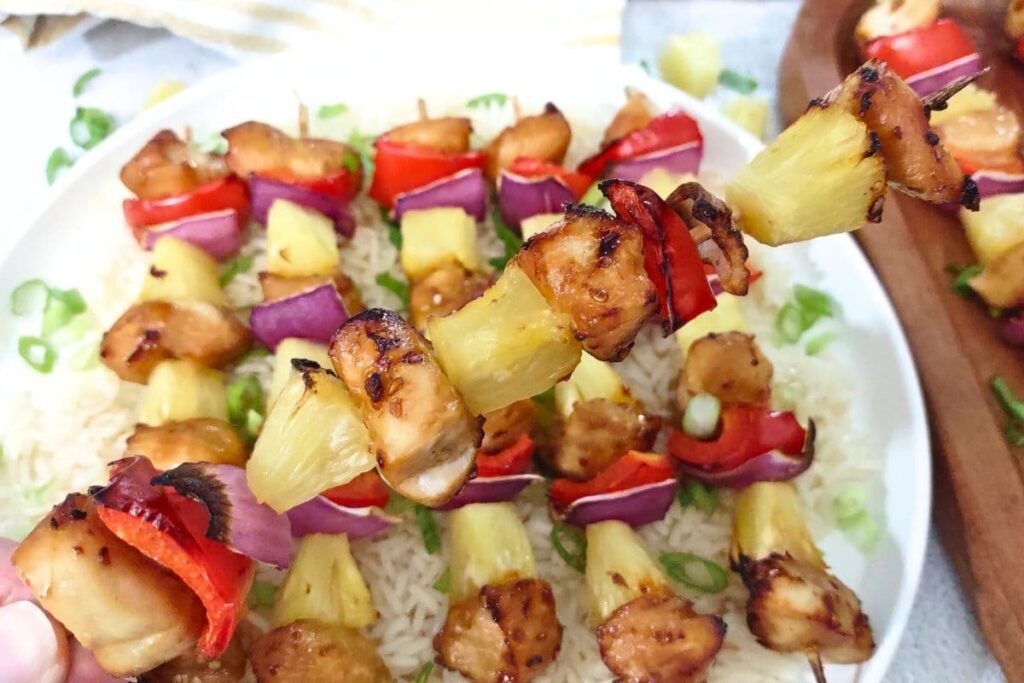 holding up a teriyaki chicken skewer with pineapple, onion, and pepper