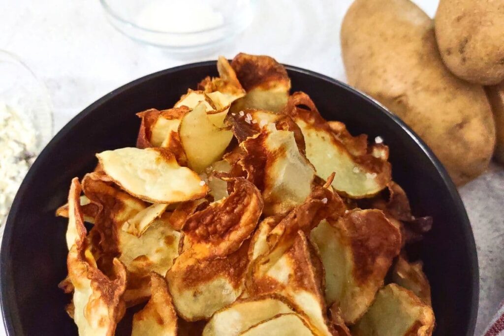 ninja air fryer potato chips in a bowl next to two fresh potatoes