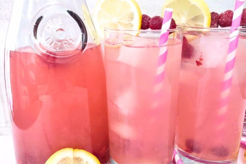 two glasses of raspberry vodka lemonade next to a pitcher