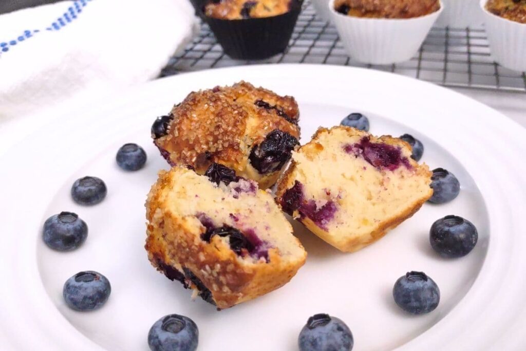 air fryer blueberry muffin split in half on a plate surrounded by fresh blueberries