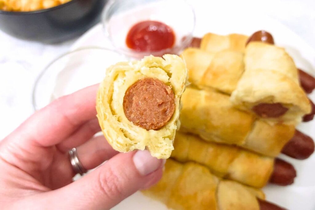 holding up a cut in half air fryer crescent roll hot dog