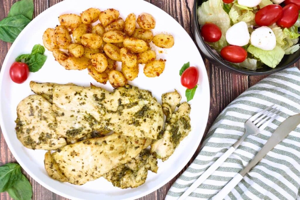 overhead view of air fryer pesto chicken on a plate with sides and a side salad